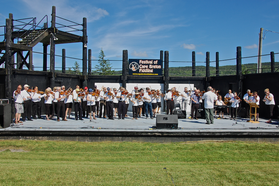 The Cape Breton Fiddlers’ Association plays its second group number in tribute, directed by Eddie Rogers and accompanied by Susan MacLean on keyboard
