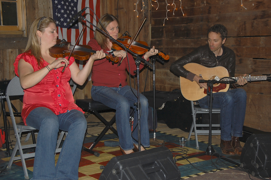 Photo of Andrea Beaton and Wendy MacIsaac on fiddles accompanied by Seph Peters on guitar