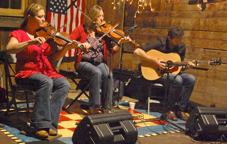 Photo of Andrea Beaton and Wendy MacIsaac on fiddles accompanied by Seph Peters on guitar