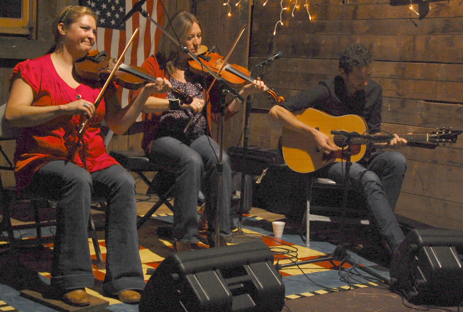 Photo of Andrea Beaton and Wendy MacIsaac on fiddles accompanied by Seph Peters on guitar
