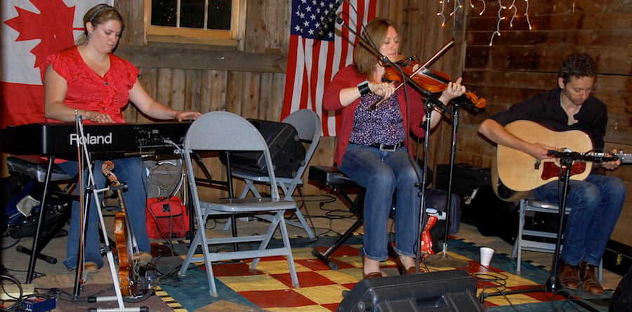 Photo of Andrea Beaton and Wendy MacIsaac on fiddles accompanied by Seph Peters on guitar